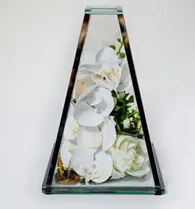 Triangular glass vase containing yellow and white roses with green foliage inside.
