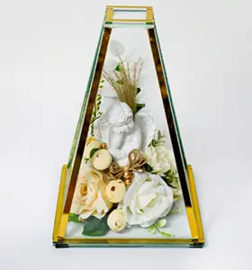 Glass pyramid container with gold edges holding a white cherub statue surrounded by artificial white roses and small beige buds.