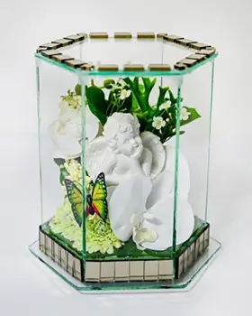 Glass hexagonal case containing a white cherub figurine surrounded by white and blue roses, green leaves, and a heart-shaped plaque with a message.