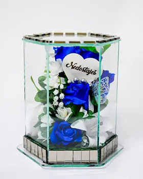Hexagonal glass container with delicate artificial flowers including roses and orchids inside.