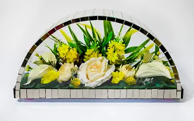 Floral arrangement with peach roses, small orange flowers, and green foliage in a half-circle mirrored frame.
