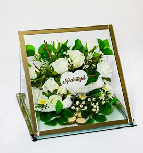 Decorative arrangement of cream-colored roses and green foliage with a small white cherub statue inside a tilted golden frame.