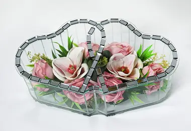 Double heart-shaped glass vase with mirrored edges containing red and white flowers and green foliage.