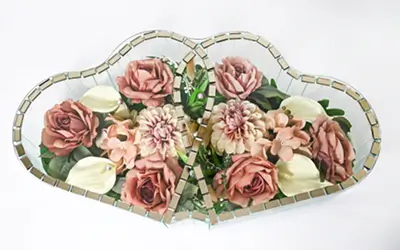 Heart-shaped mirrored decoration with white and dark red roses inside and green leaves.