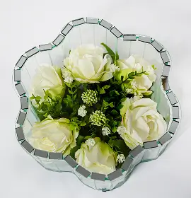 Decorative glass vase shaped like a flower containing artificial pink roses and greenery.
