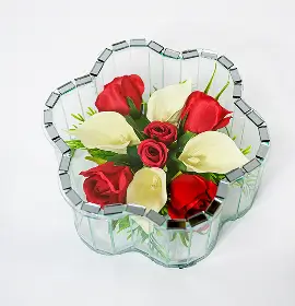 Glass vase shaped like a flower filled with white roses and green foliage.