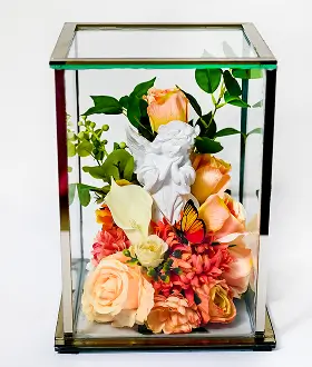Glass box with golden frame containing a bouquet of red roses, white lilies, and small white flowers with green leaves.