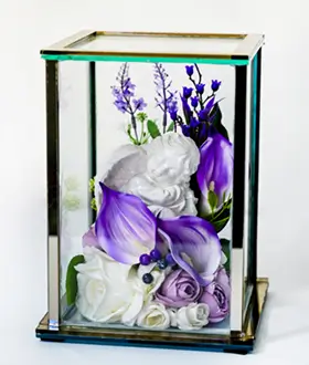 Glass display case holding a white angel figurine surrounded by peach and pink flowers with green leaves and a yellow butterfly.