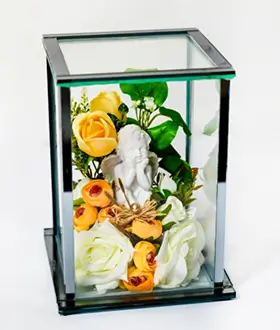 Glass display case with gold edges containing a white angel figurine surrounded by red and white roses and green foliage.