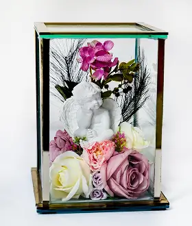 Glass case containing a white cherub figurine surrounded by purple and white flowers with green leaves and small blue berries.