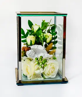 Glass display case with white roses, green berries, and other greenery arranged inside.