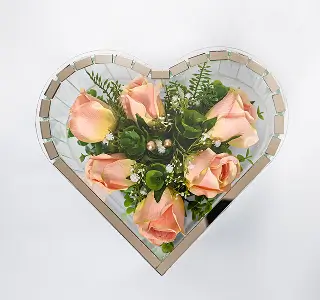Heart-shaped floral arrangement with six peach roses and green foliage inside a mirrored mosaic frame.