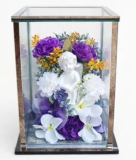 Decorative glass and brass terrarium containing artificial flowers, including cream and dark red roses with green leaves.