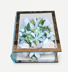 Glass box with golden frame containing a bouquet of red roses, white lilies, and small white flowers with green leaves.