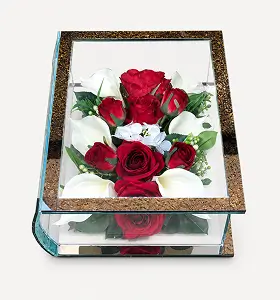 Glass shadow box containing a floral arrangement with red roses, white lilies, and green foliage.