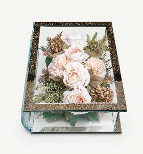 Glass shadow box containing a floral arrangement with red roses, white lilies, and green foliage.