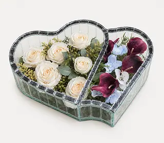 Two heart-shaped glass compartments with mirrored edges, one filled with red roses and the other with white roses and greenery.