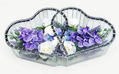 Heart-shaped mirrored decoration with white and dark red roses inside and green leaves.