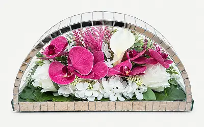 White angel figurine surrounded by white roses and greenery inside a dome-shaped glass enclosure with a gold and green border.