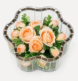 Glass flower-shaped vase with gold trim holding pink roses and green foliage.