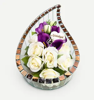 Tear-drop shaped mirror frame surrounding a flower arrangement of purple and white flowers with a decorative plaque in the center.