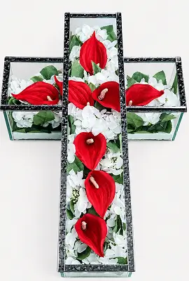 Silver cross with pink roses and green foliage arranged inside it.