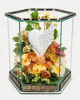 Glass rectangular display box with brass frame containing artificial flowers including white lilies, cream roses, and pink blossoms on a white surface.