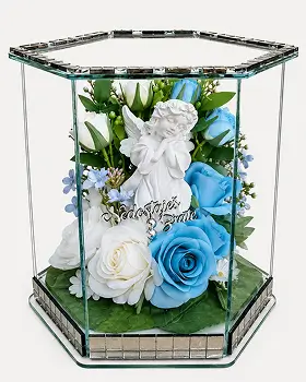 Glass rectangular display box with brass frame containing artificial flowers including white lilies, cream roses, and pink blossoms on a white surface.