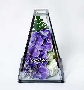 White orchid and rose flowers displayed inside a clear glass pyramidal vase against a plain white background.