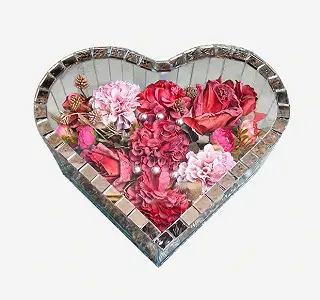 Glass rectangular display box with brass frame containing artificial flowers including white lilies, cream roses, and pink blossoms on a white surface.