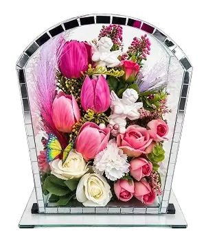 Glass pyramid display containing a white figurine surrounded by cream roses and green leaves.