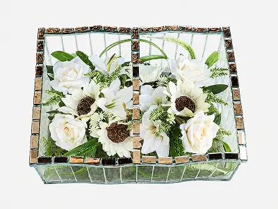 Glass container with two compartments holding red roses, white lilies, and green foliage on a white background.