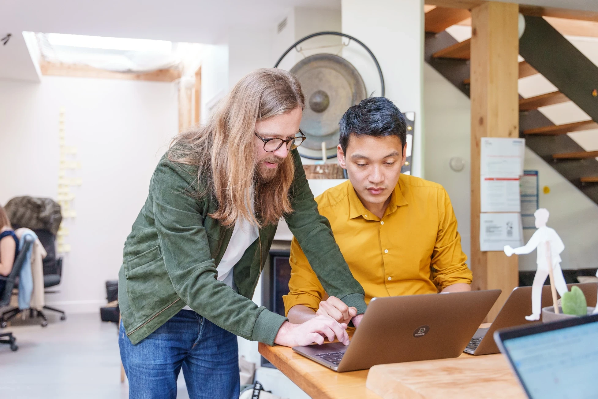 Deux hommes collaborant sur un ordinateur portable dans un espace de travail moderne.
