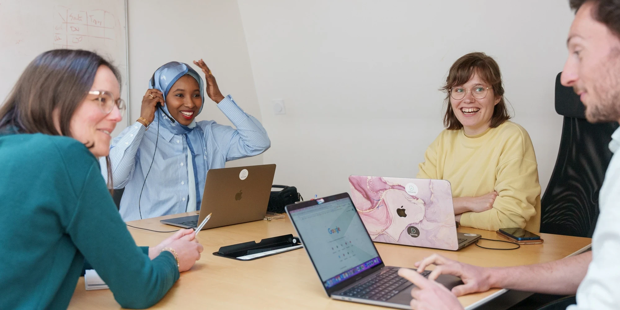 Quatre collègues souriants discutent lors d'une réunion autour d'une table avec des ordinateurs portables.