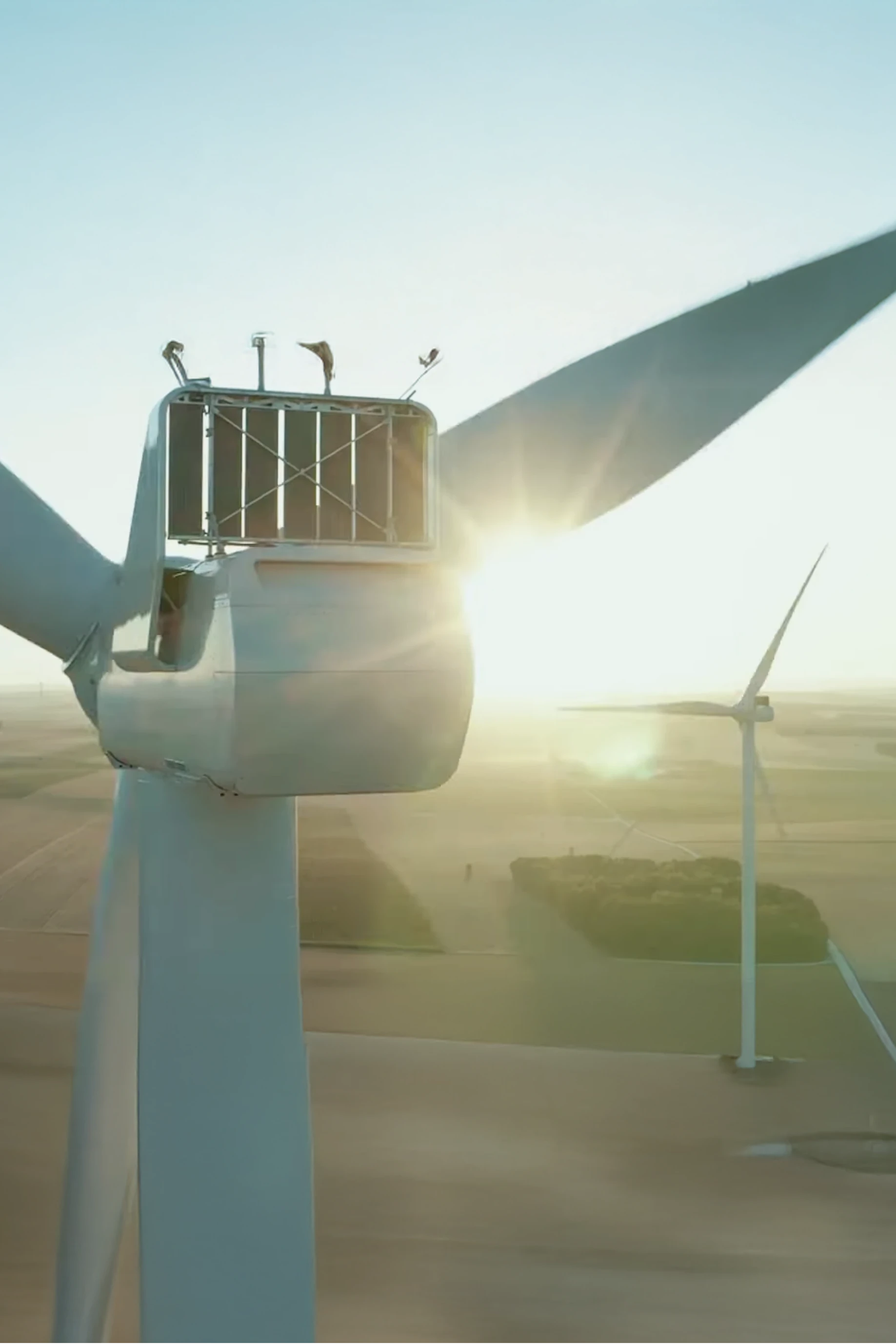 Gros plan sur une éolienne avec le soleil se levant à l'arrière-plan dans un paysage rural.