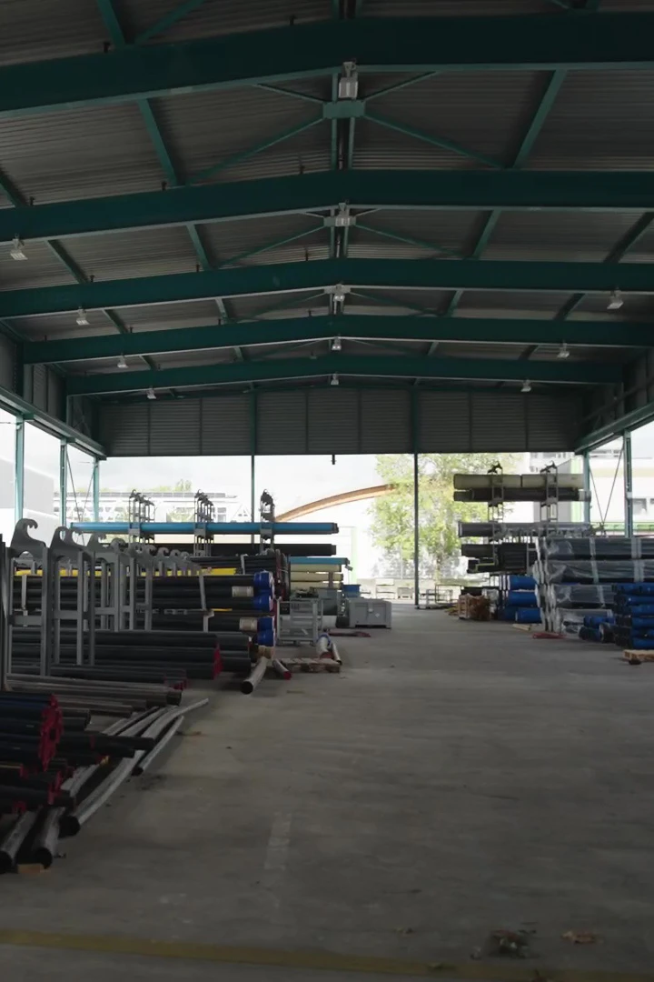 Entrepôt industriel avec des rangées de tuyaux métalliques empilés sur des palettes sous une grande structure en acier.