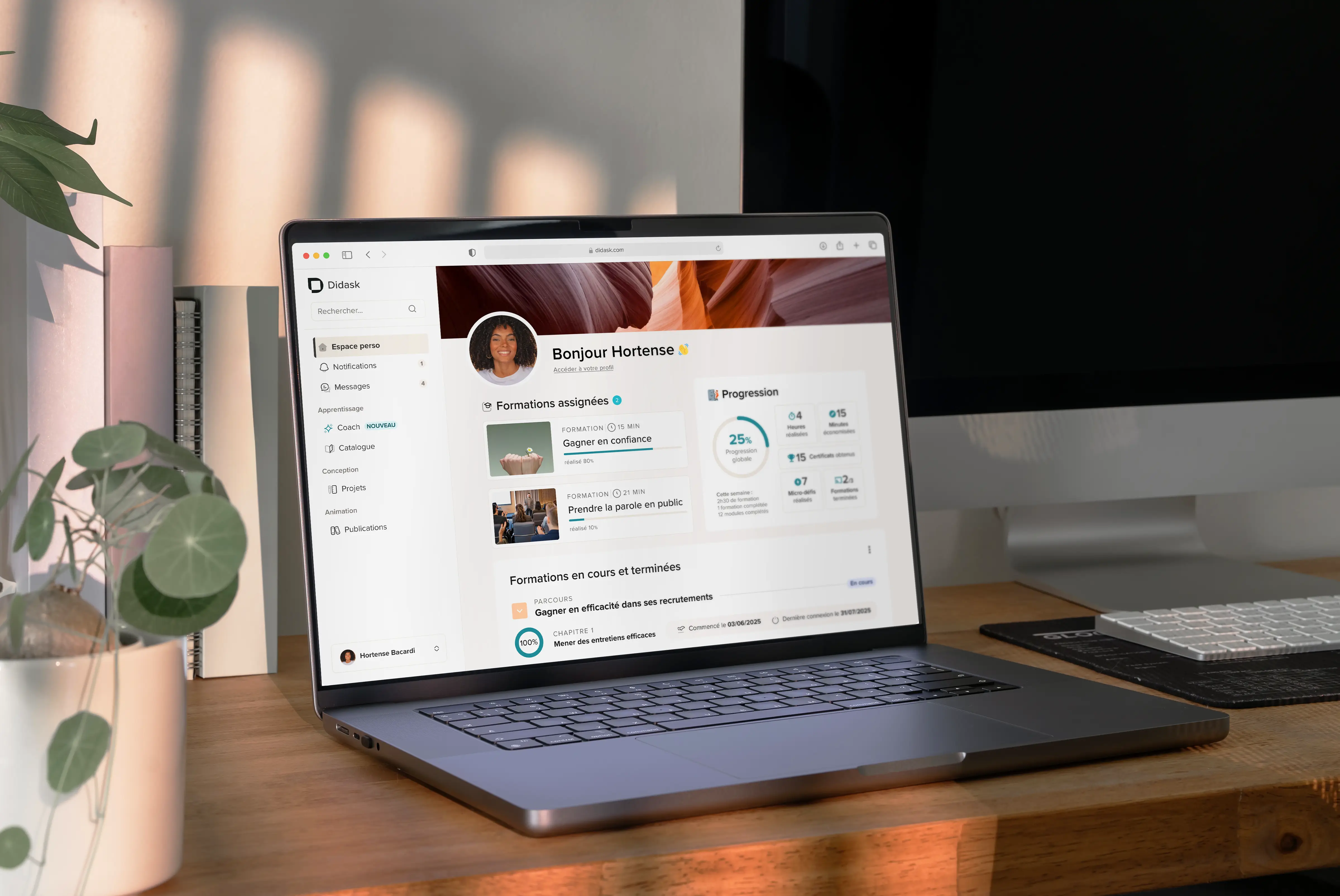 Ordinateur portable affichant un tableau de bord de formation en ligne avec les progrès et les cours assignés, posé sur une table en bois à côté d'un carnet orange.