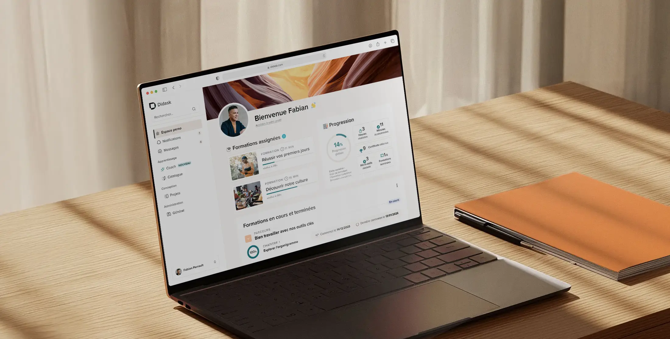Ordinateur portable affichant un tableau de bord de formation en ligne avec les progrès et les cours assignés, posé sur une table en bois à côté d'un carnet orange.