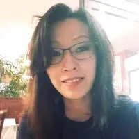 Portrait d'une femme souriante aux cheveux longs et lunettes, avec un fond intérieur flou.