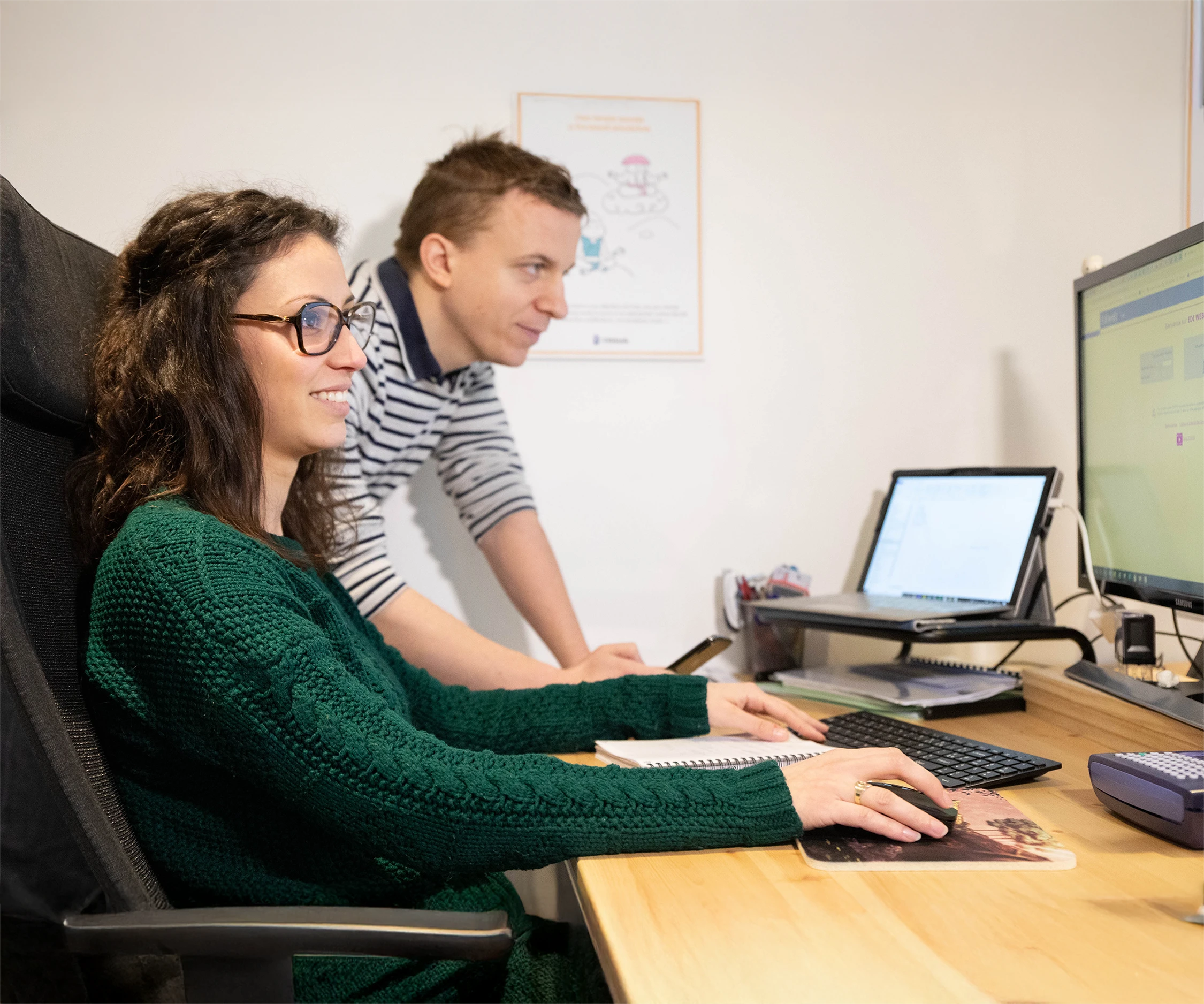 Deux personnes travaillant ensemble devant un ordinateur, une femme au premier plan utilise une souris tandis qu'un homme la regarde.