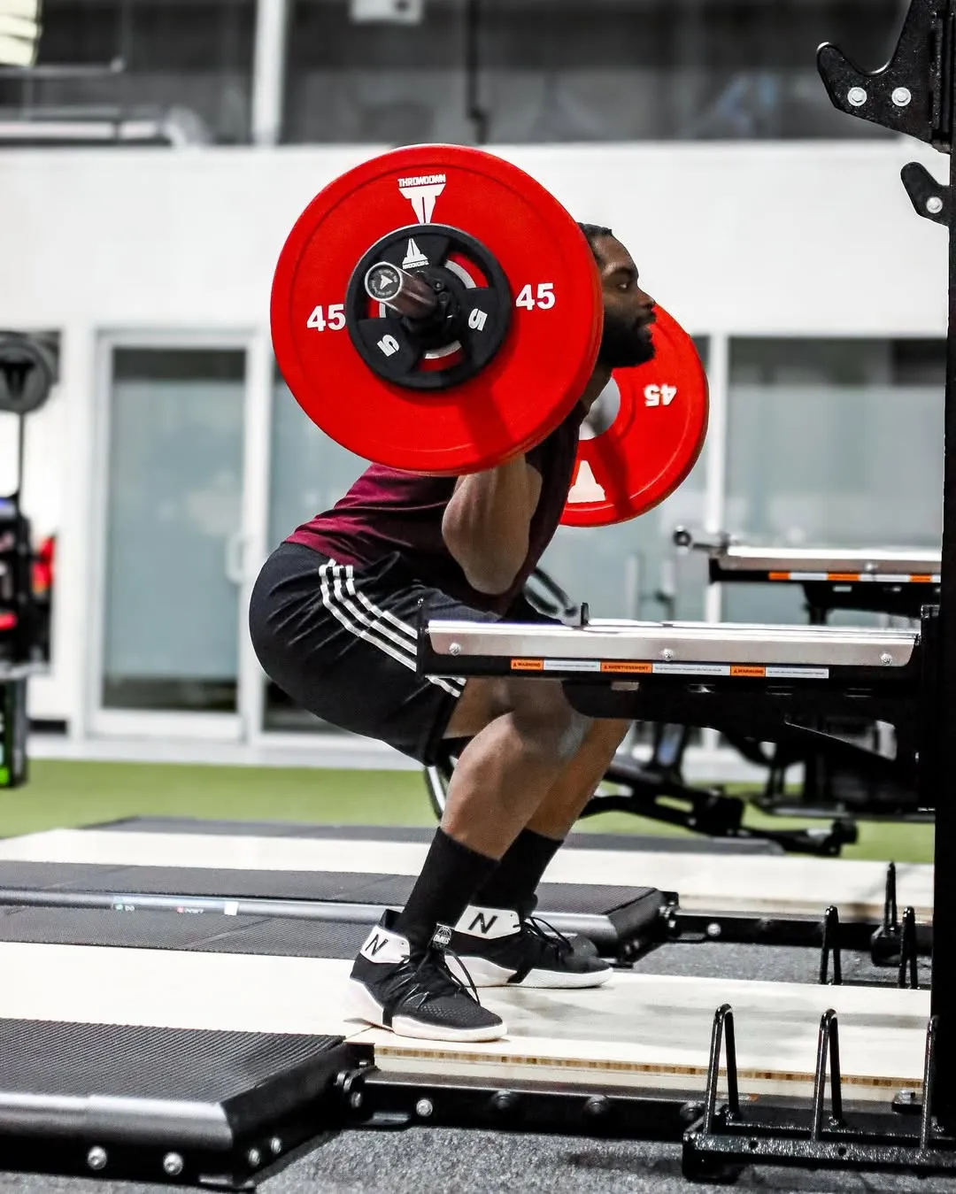 Man performing a barbell back squat with 45-pound red weight plates in a gym.