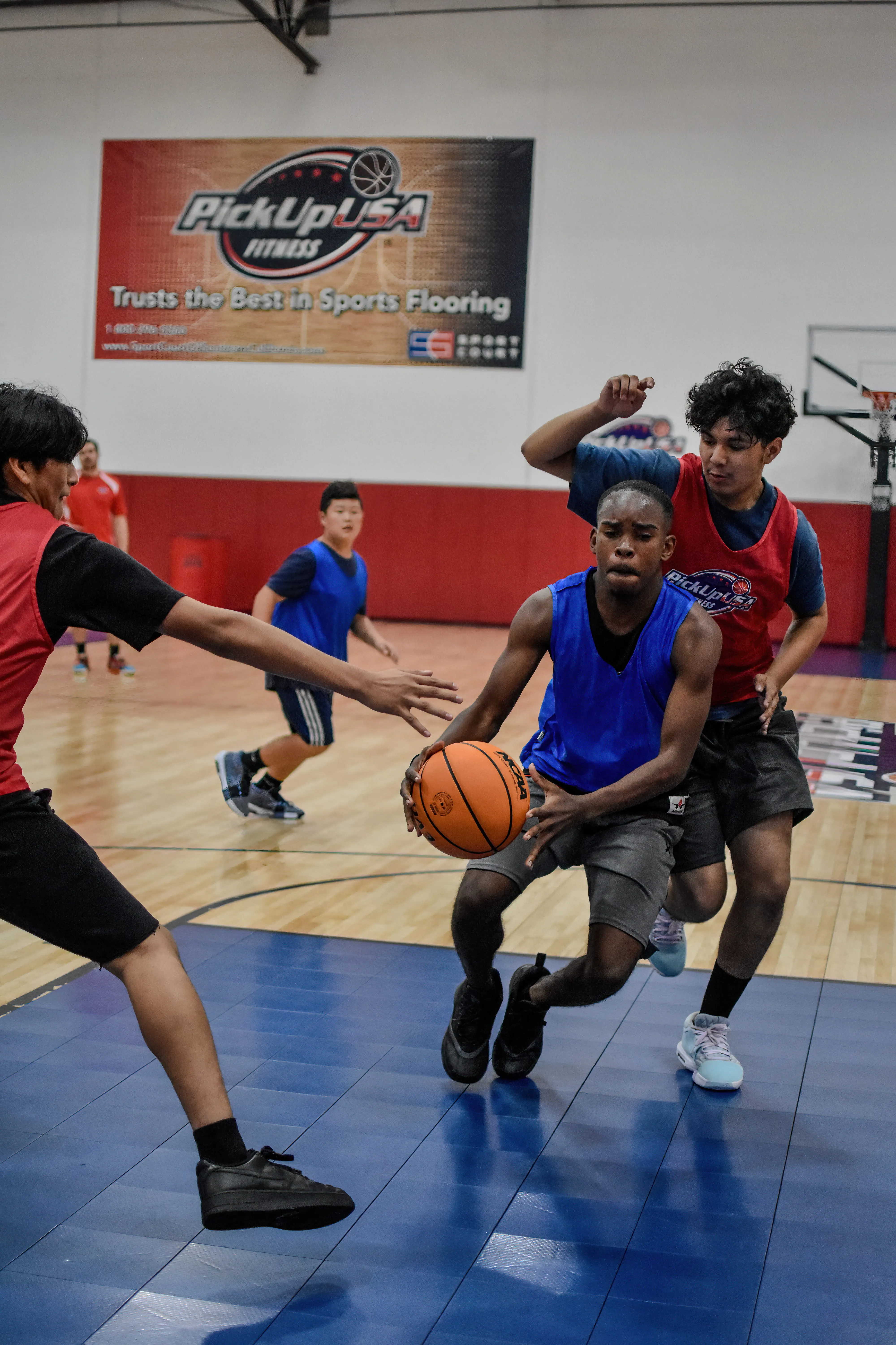 Teen basketball players in blue and red jerseys competing on an indoor court.