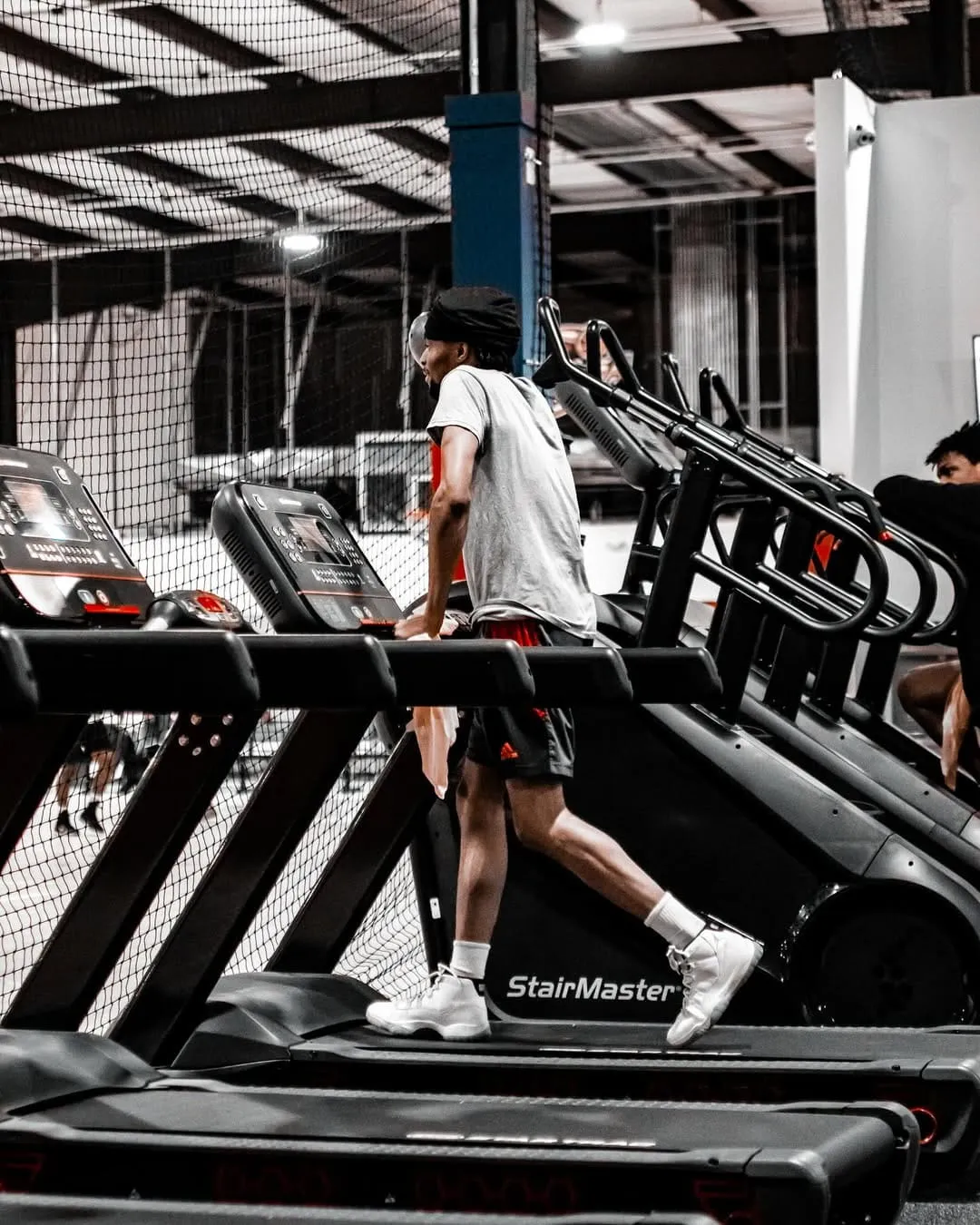Person walking on a treadmill inside a gym with multiple StairMaster machines nearby.