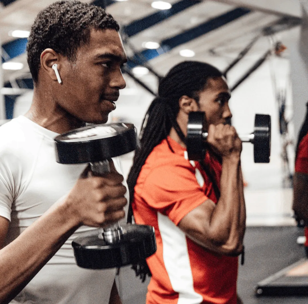 Two men lifting dumbbells performing bicep curls in a gym.