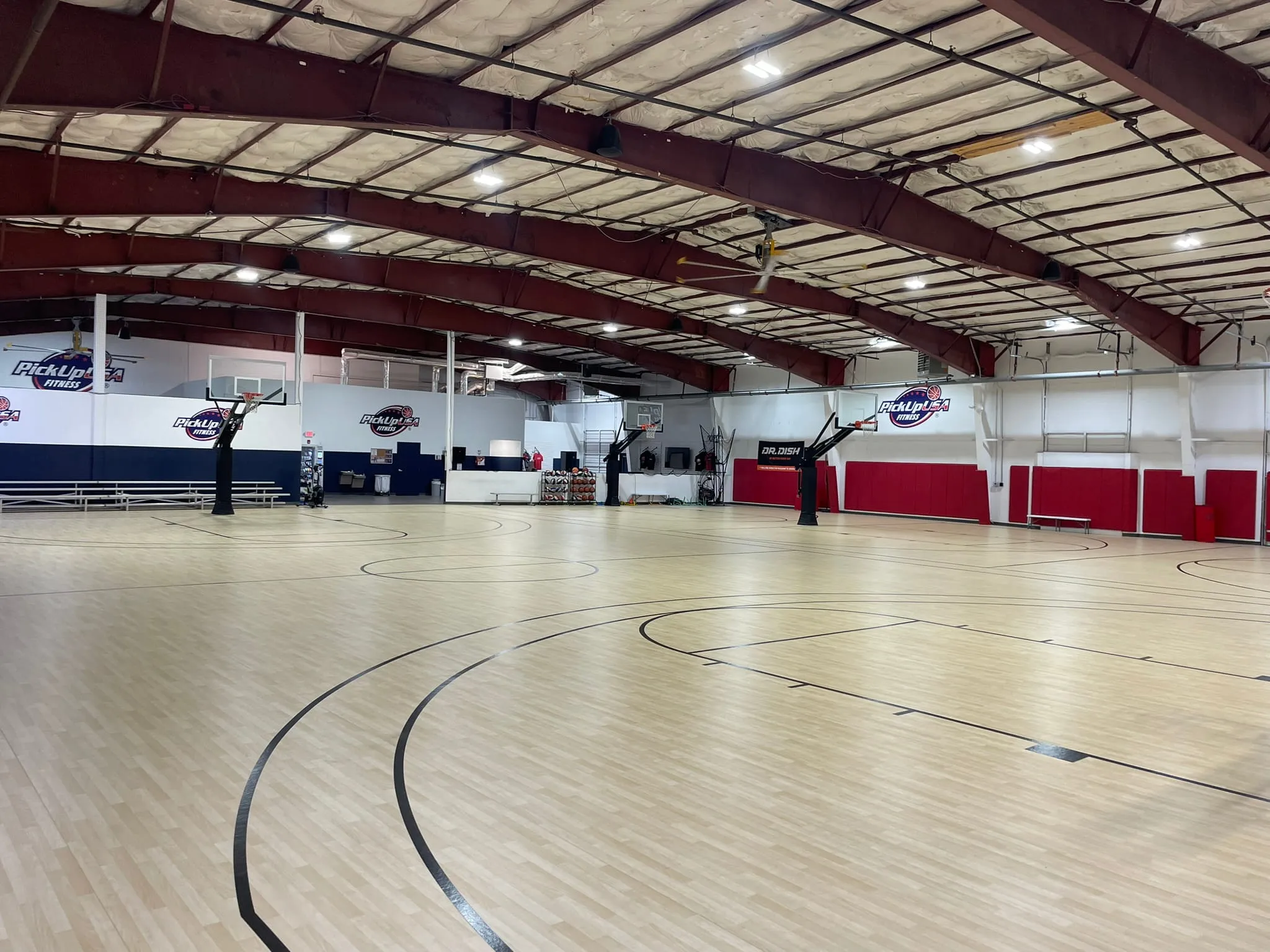 Spacious indoor basketball court with multiple hoops, light wood flooring, and PickUpUSA Fitness logos on the walls.
