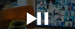 Coffee cup on desk next to a laptop screen showing a video call with multiple participants.