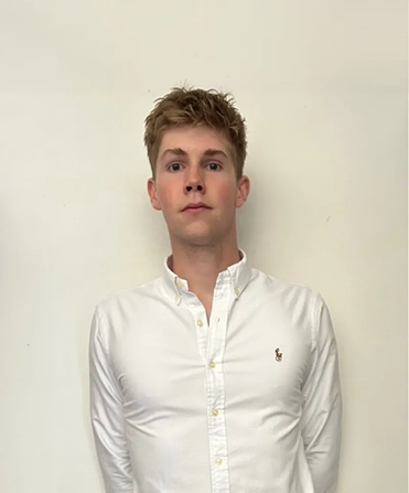 Young man with short tousled hair wearing a white button-up shirt against a plain light wall.