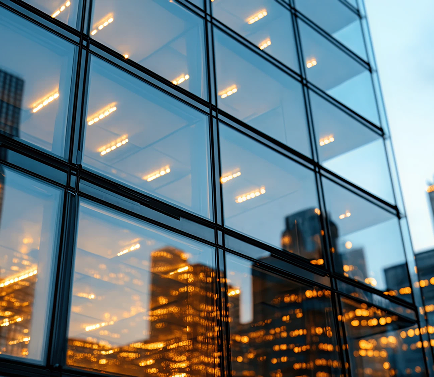 Reflection of illuminated city skyscrapers on the glass windows of a modern building at dusk.
