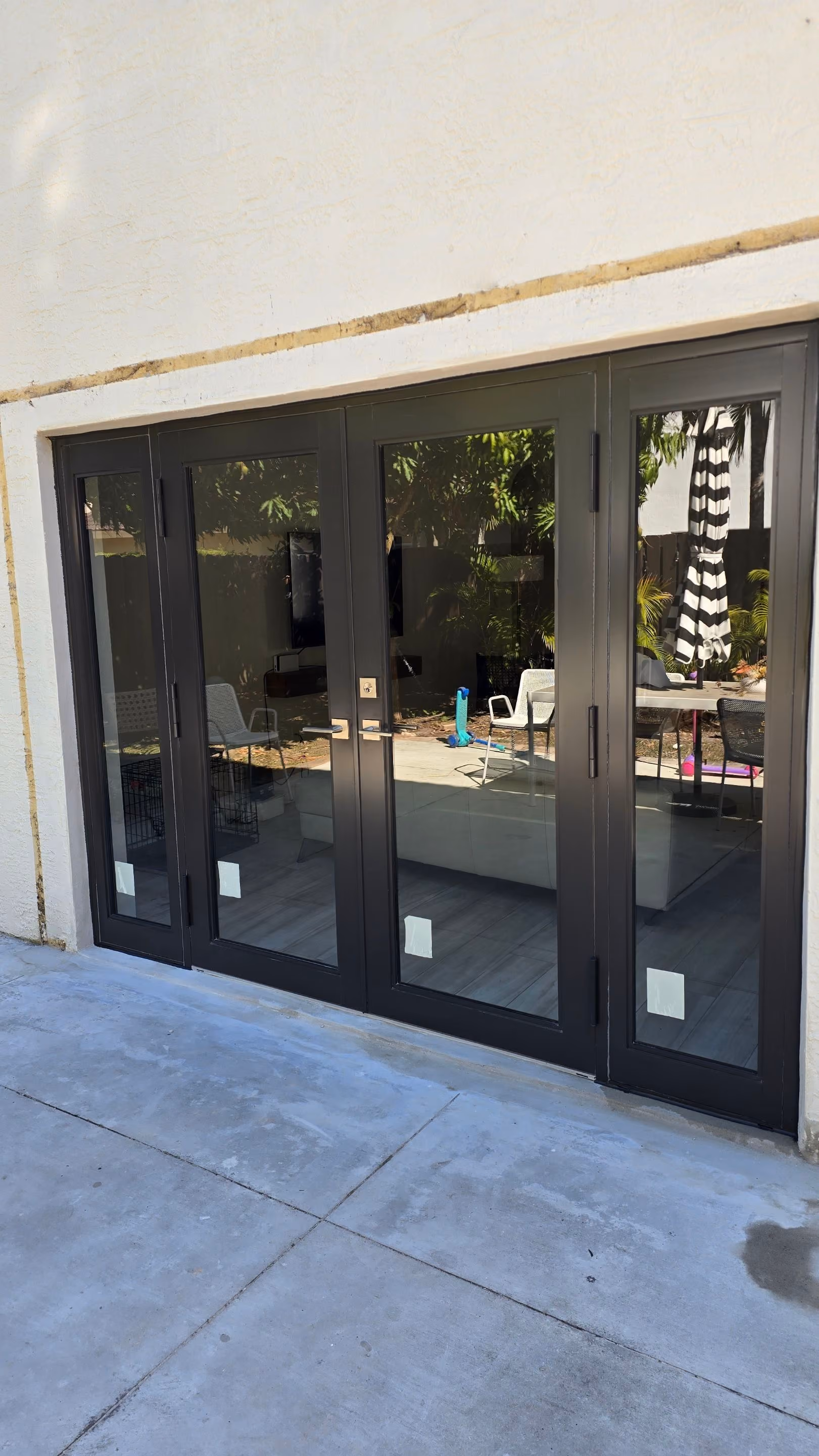 Black french doors reflecting outdoor furniture, plants, and a striped umbrella.