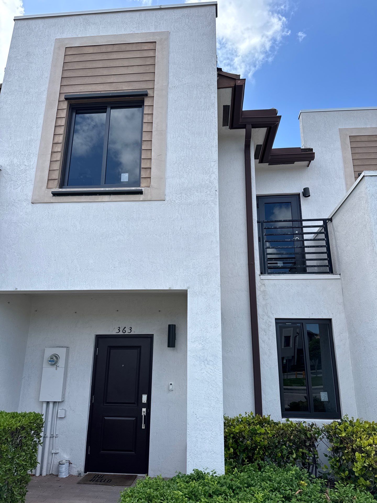 Modern white two-story house with black front door numbered 363, large windows, and trimmed green bushes.